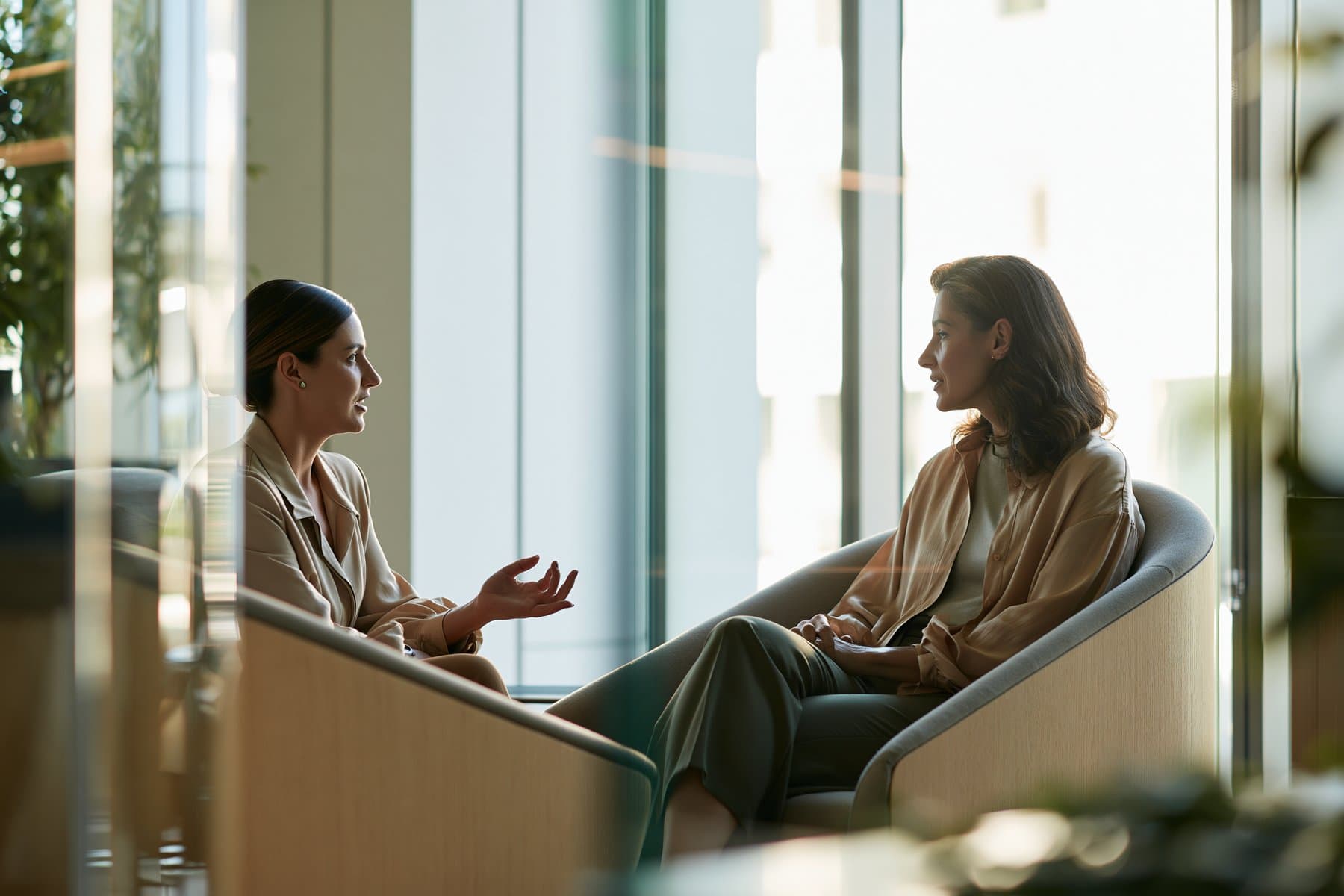 Two people in a calm conversation in lounge chairs by a tall window